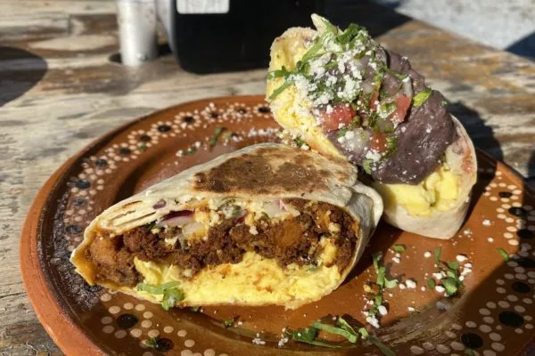 Two breakfast burritos cut in half and stacked, one full of chorizo and egg and the other full of beans and eggs. The burritos are on a brown patterned plate on a wooden table. | 1010 White Street SW, Atlanta, GA 30310