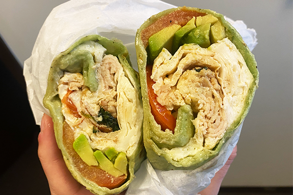 Breakfast burrito in a green wrap sliced in half and displayed to the camera, full of deli meat, avocado, tomato, and more | 1544 Piedmont Avenue North East Suite 203, Atlanta, GA 30324