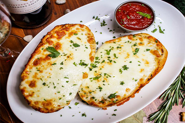 Two slices of cheesy garlic bread topped with green herbs on a white plate with a side of marinara sauce | 230 Peachtree St NW, Atlanta, GA