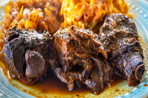 Three braised oxtails on a blue plate with cabbage and macaroni and cheese in background | 1583 S Lumpkin St, Athens, GA 30605