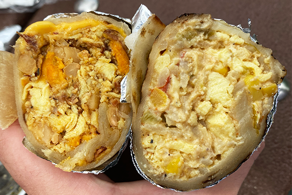 Two densely-packed breakfast burritos cut in half and displayed to the camera in a hand | 2233 College Ave NE, Atlanta, GA 303017