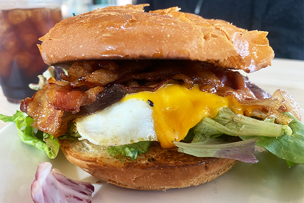 Fried egg, bacon, cheddar cheese, and greens on a soft roll on a white plate | 1460 Ellsworth Industrial Blvd NW, Atlanta, GA 30318