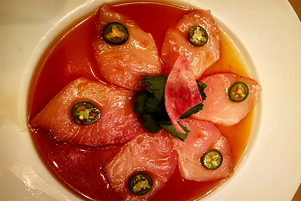 Spiraling layout of yellowtail in a marinade with sliced jalapenos on top